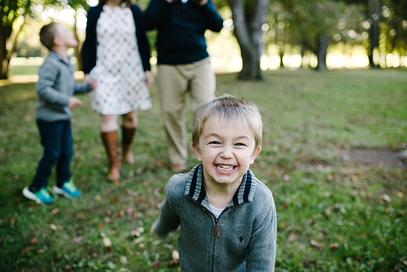little boy in grey sweater running in front of his family