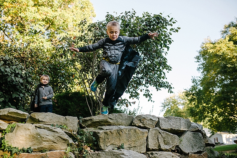 little boy in spiderman costume jumping off stone wall