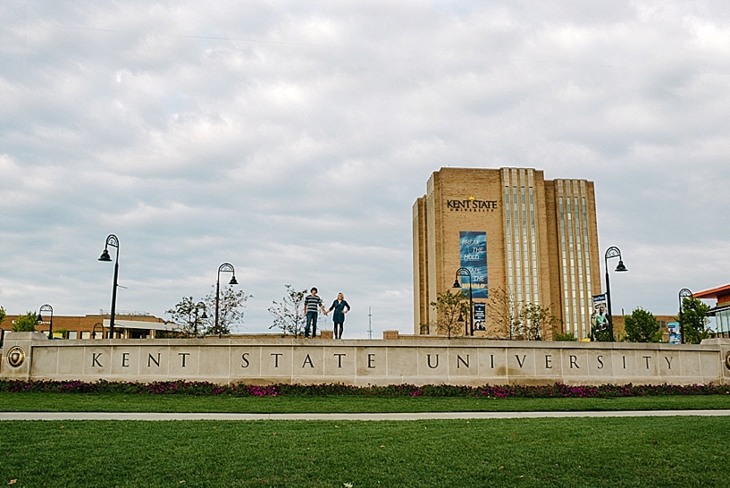 guy and girl standing on Kent State University Sign