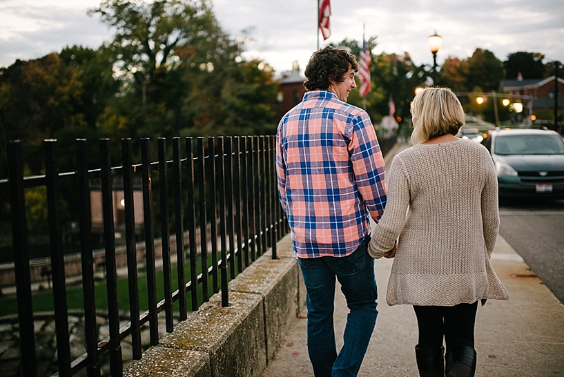 girl in oversized sweater and guy in pink and blue plaid shirt holding hands walking across bridge on busy street