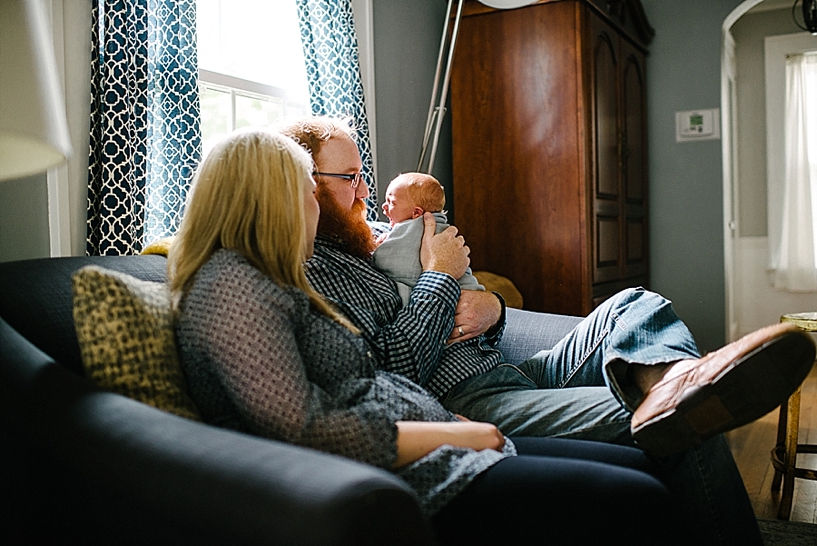 parents sitting on couch by window holding baby