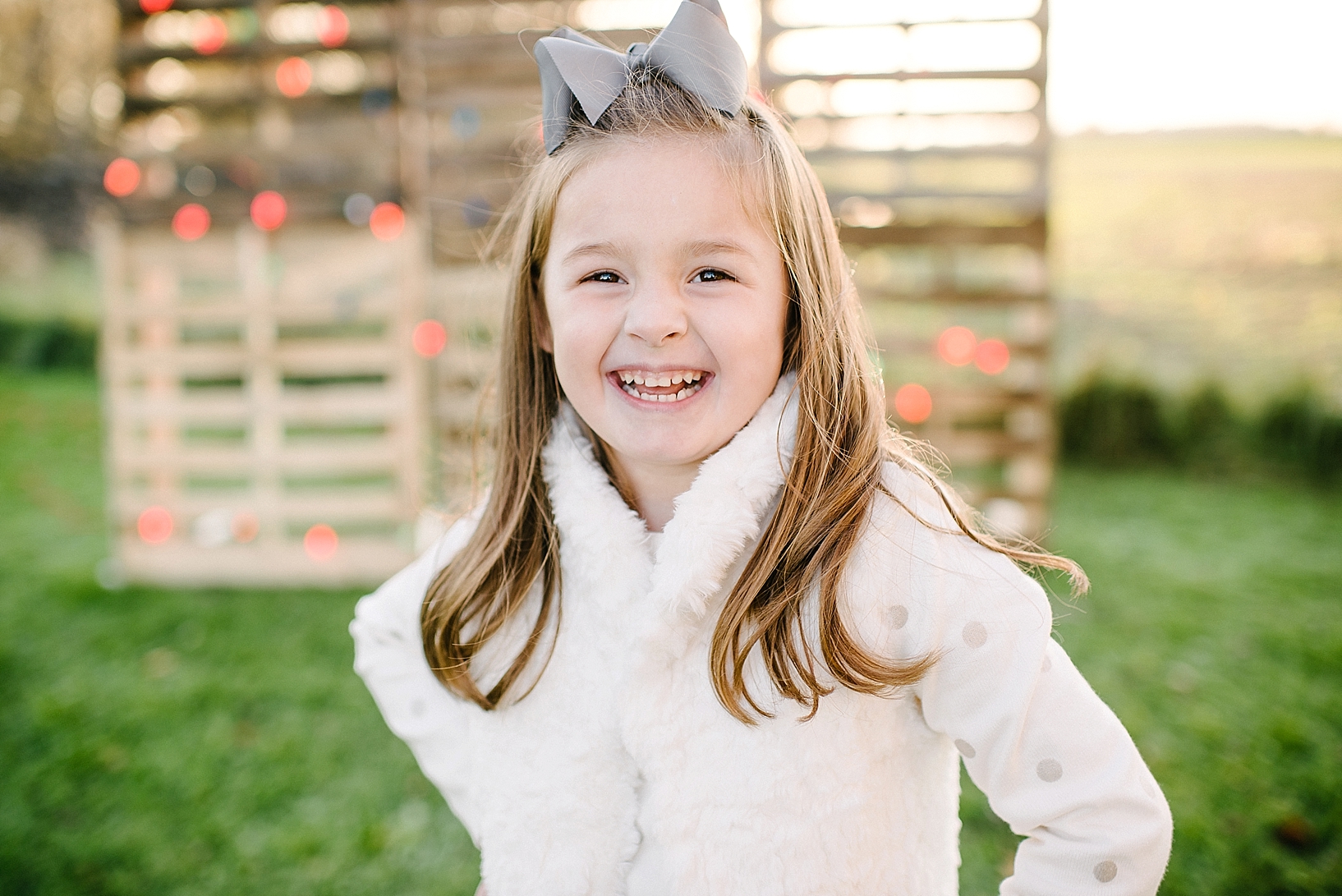 young girl wearing cream sweater standing in front of DIY pallet wall with Christmas lights