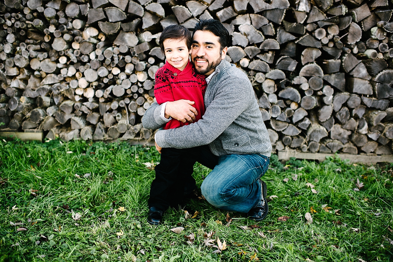 father in grey sweater hugging toddler son wearing red Christmas sweater