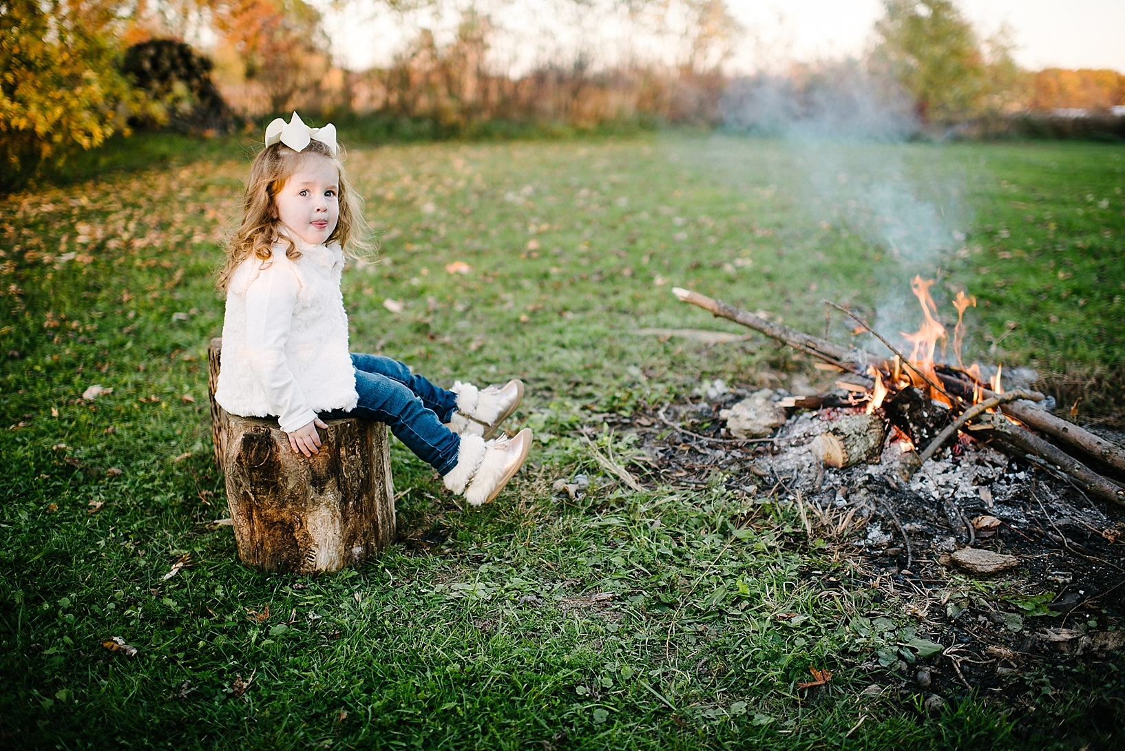 little girl sitting on tree stump by campfire