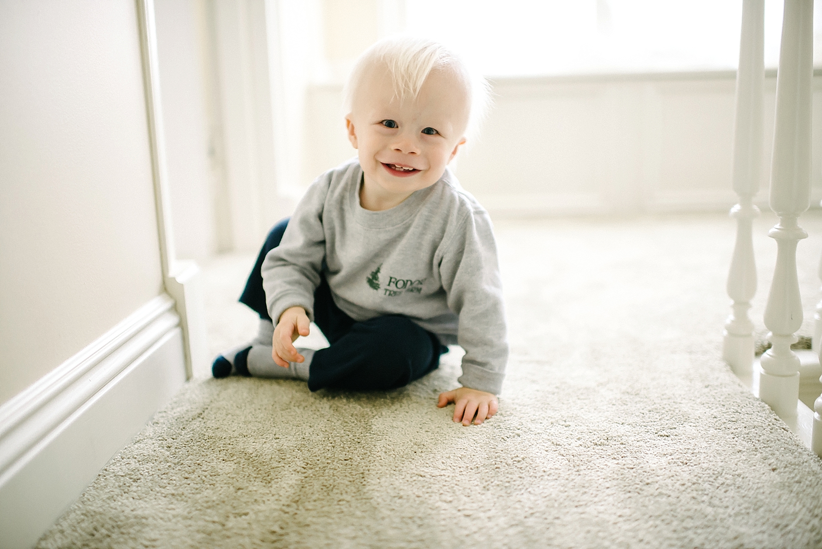 18 month old boy sitting on floor by window smiling