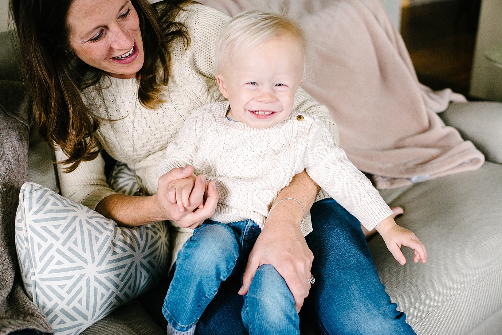 mom in cable knit sweater laughing holding toddler son on her lap on couch
