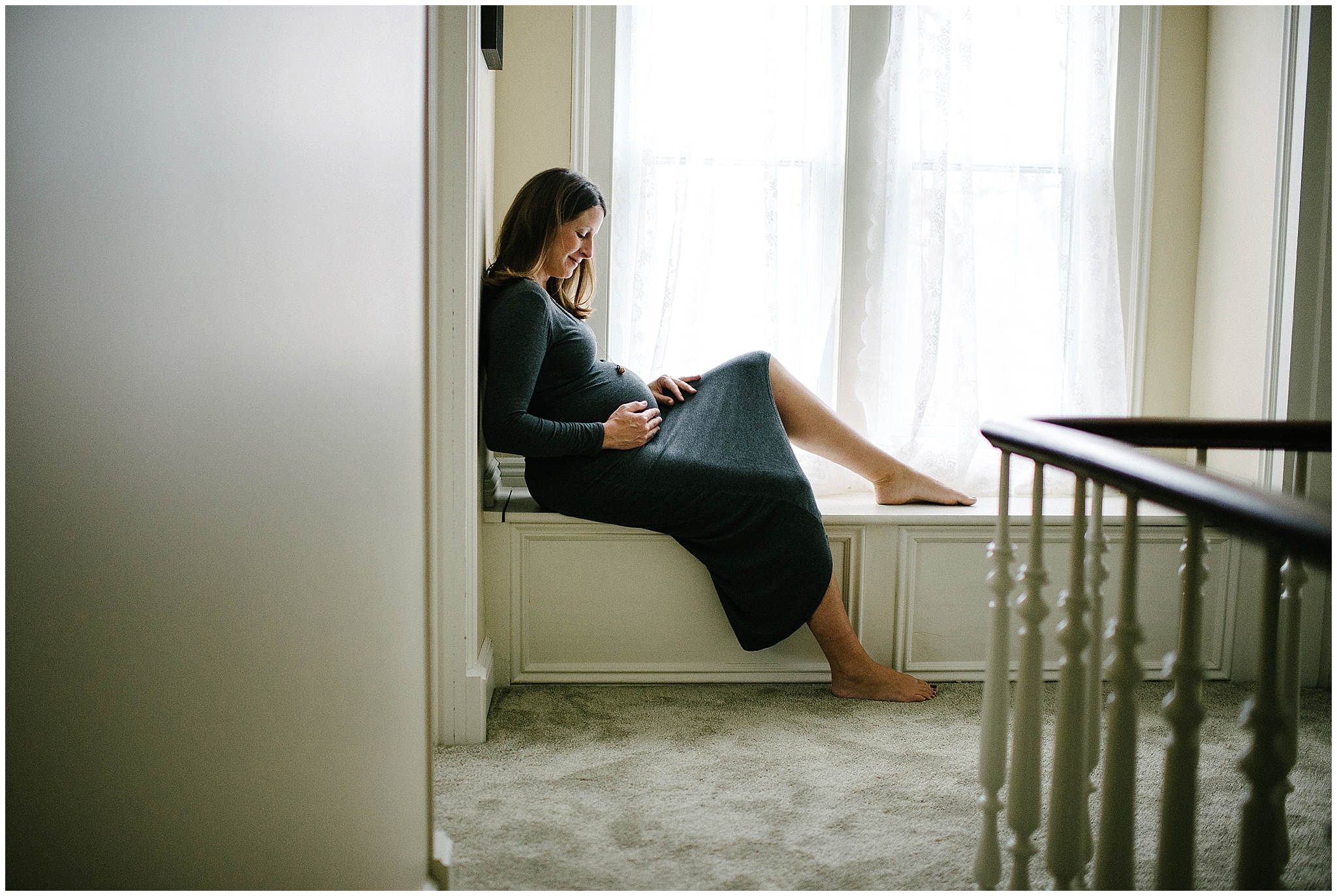 expectant mother wearing long grey dress sitting in window seat 