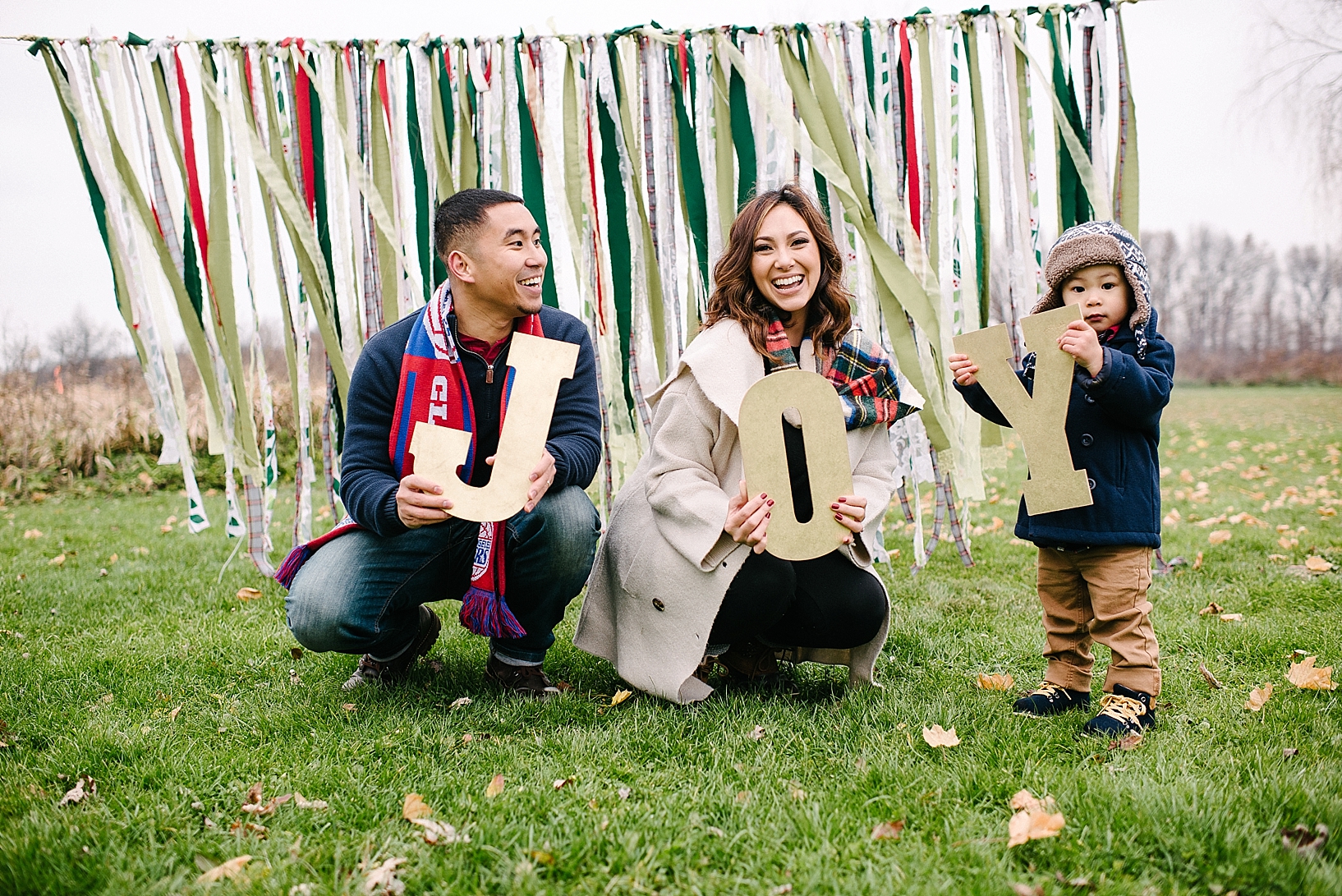 family dressed in winter coats holding JOY letters in front of streamer curtain