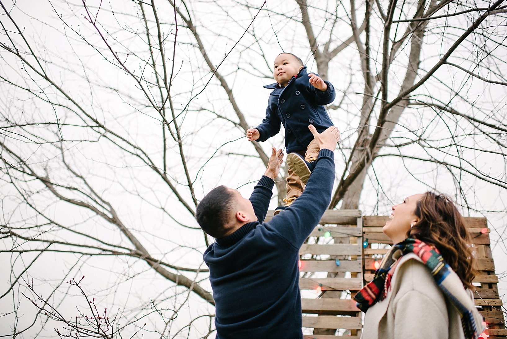 dad tossing toddler son high in the air with mom standing nearby laughing
