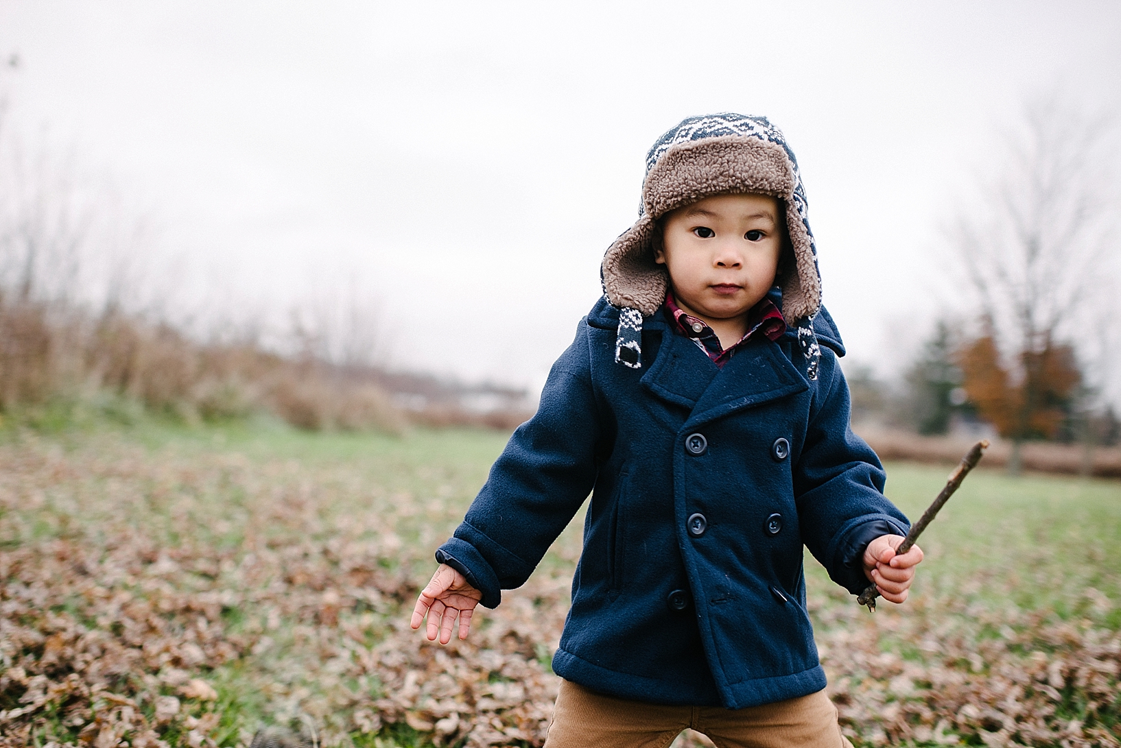 little boy wearing navy pea coat and khakis standing outside in country field in winter