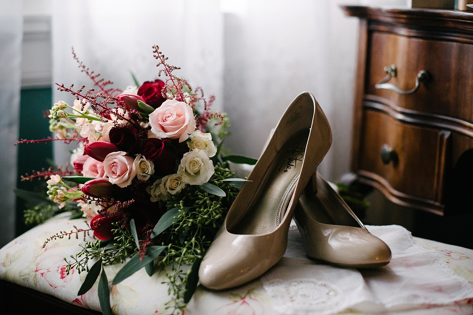 bridal bouquet with burgundy roses and nude heels sitting on vanity bench