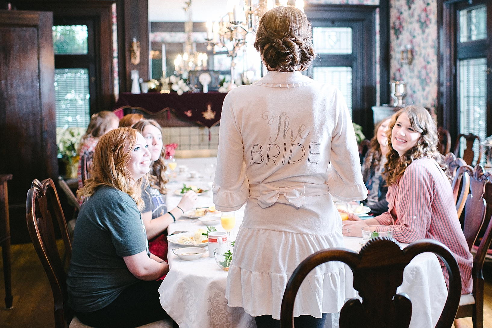 bride standing at head of table wearing Bride robe with bridesmaids eating breakfast