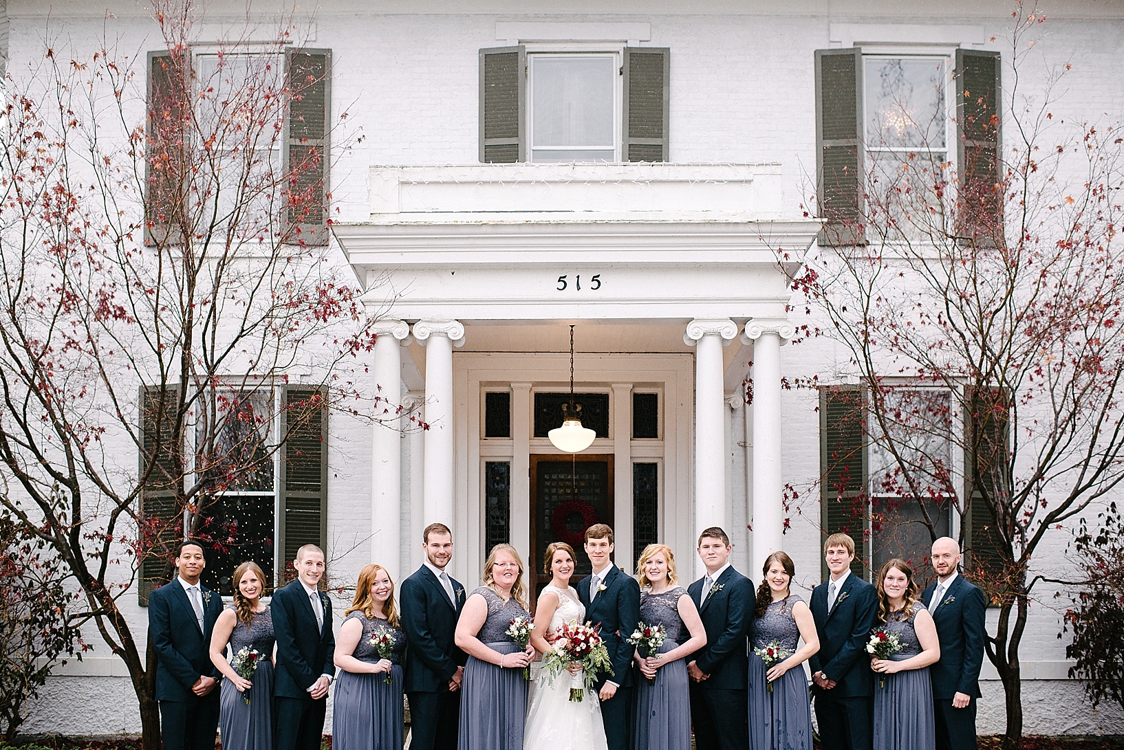 bridal party in navy and grey standing in front of white home with pillars