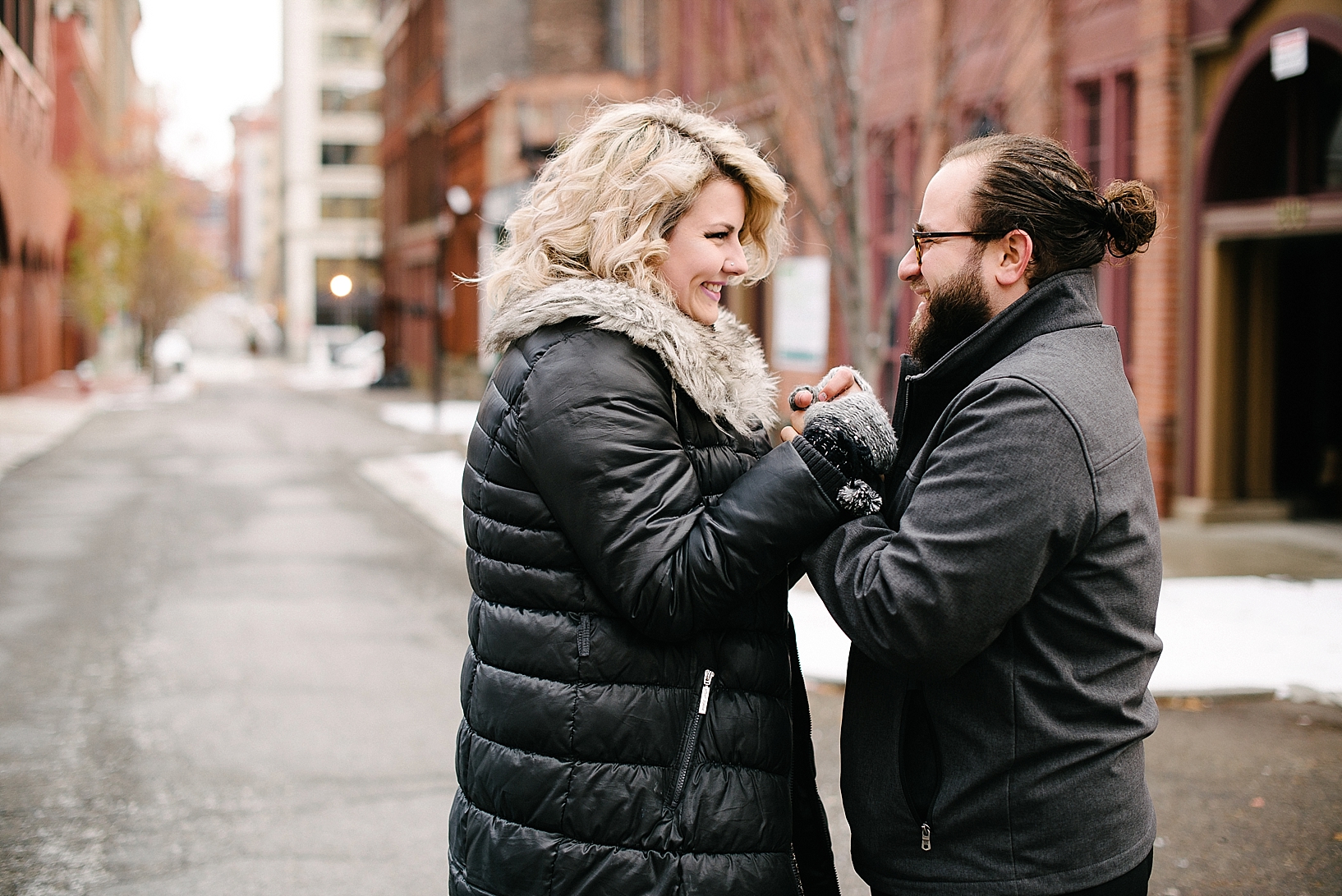 couple standing in middle of street holding hands wearing winter coats