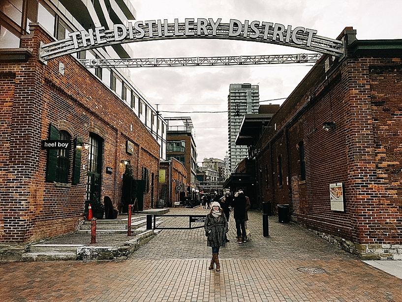 woman standing underneath The Distillery District sign 