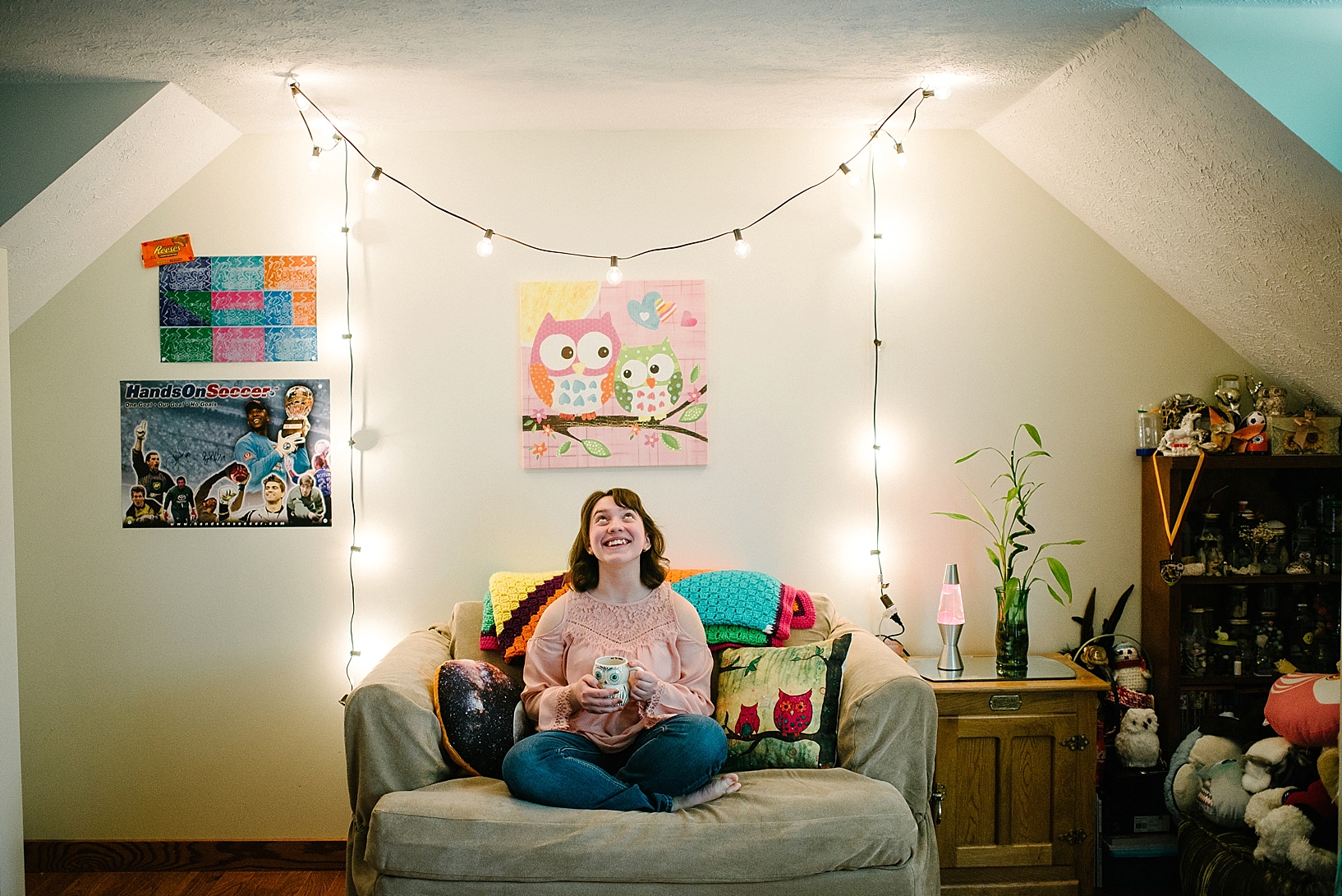 teen girl sitting on couch in bedroom with string lights on the wall drinking coffee and laughing