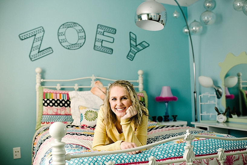 teen girl laying on colorful bedspread in teal room with Zoey in metal letters hanging on wall
