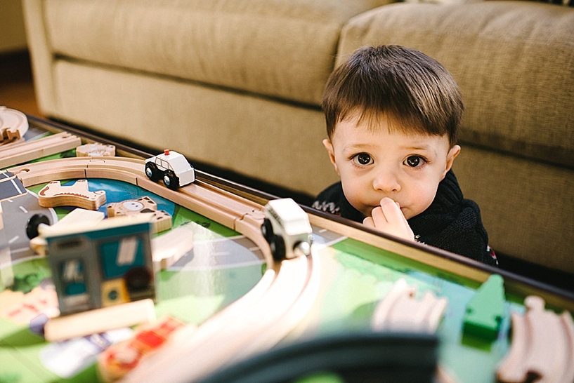 toddler boy with big brown eyes playing by train table
