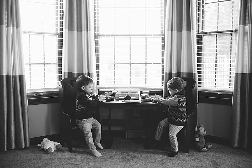 twin toddler boys sitting at table playing in front of big windows in living room