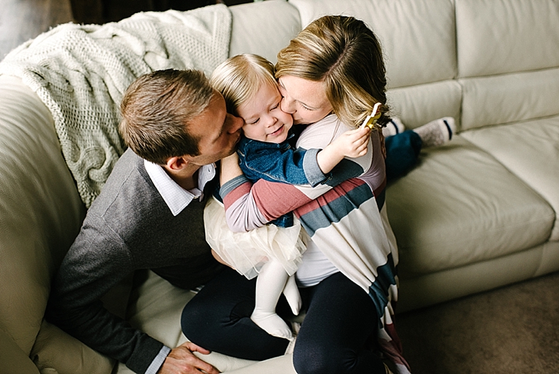 mom and dad hugging toddler daughter on couch