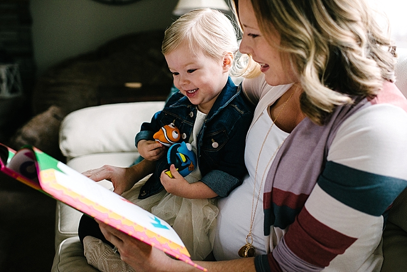 pregnant mother holding toddler daughter on her lap reading a book