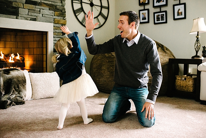 dad gives little girl wearing denim jacket and dress high five in living room