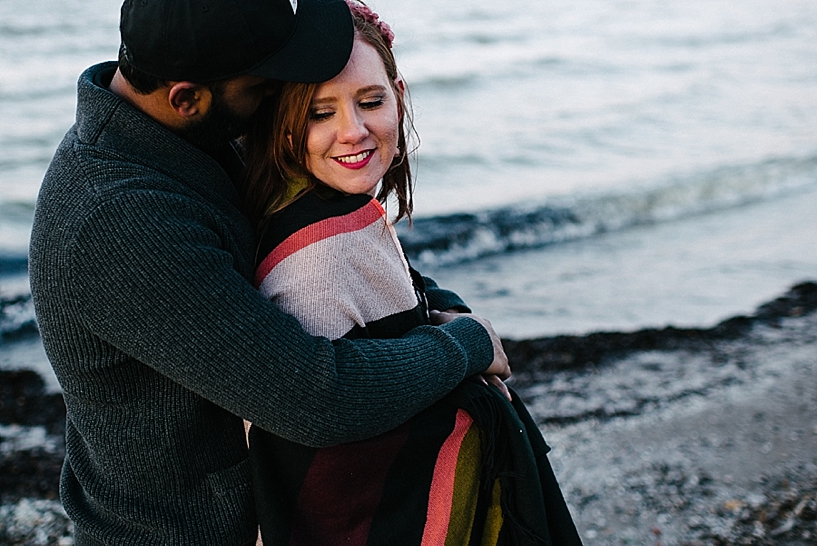 man in black sweater hugging woman with blanket wrapped around her standing by Lake Erie