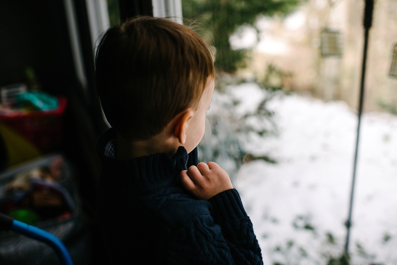 little boy looking outside window with snow on the ground