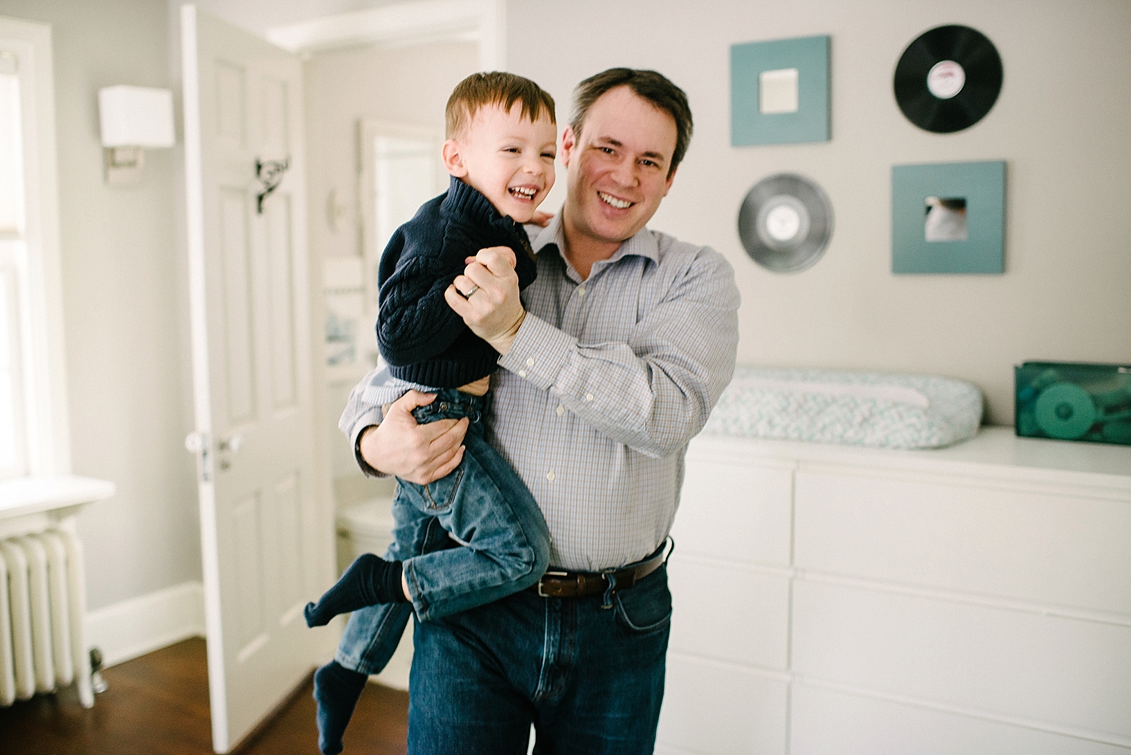dad in plaid button down shirt holding son in arms dancing in bedroom