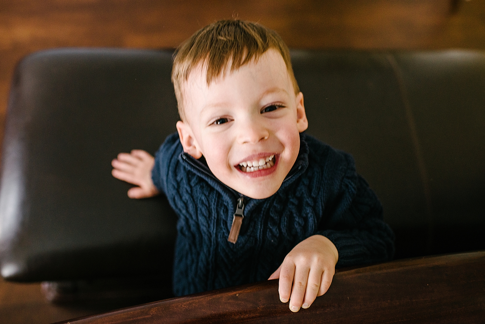 young boy wearing blue sweater smiling up at camera in bedroom