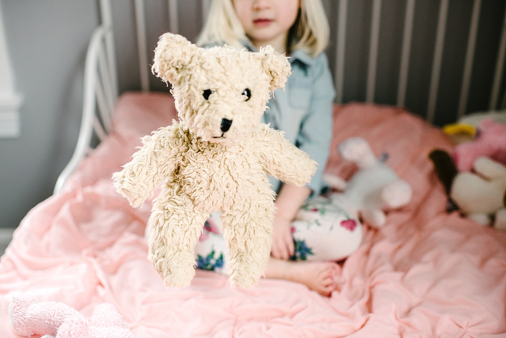 toddler girl holding teddy bear sitting on her bed