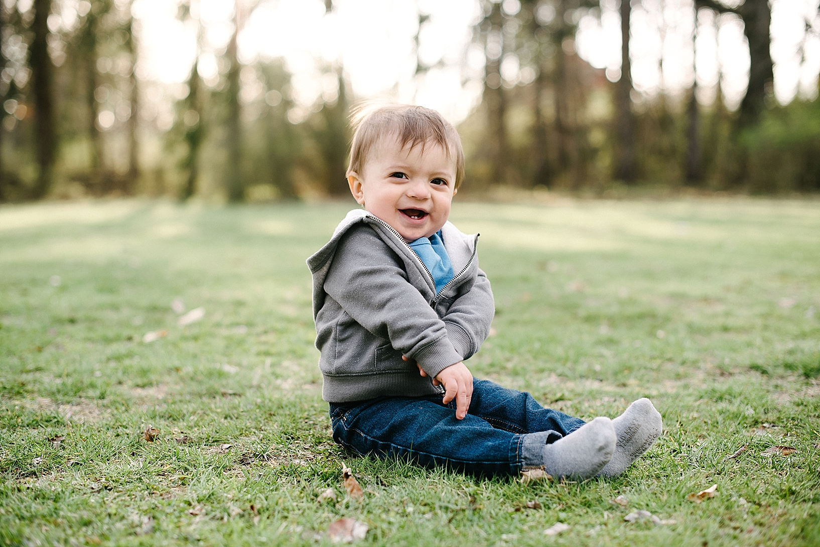 one year old boy sitting in grass wearing jeans and hoodie