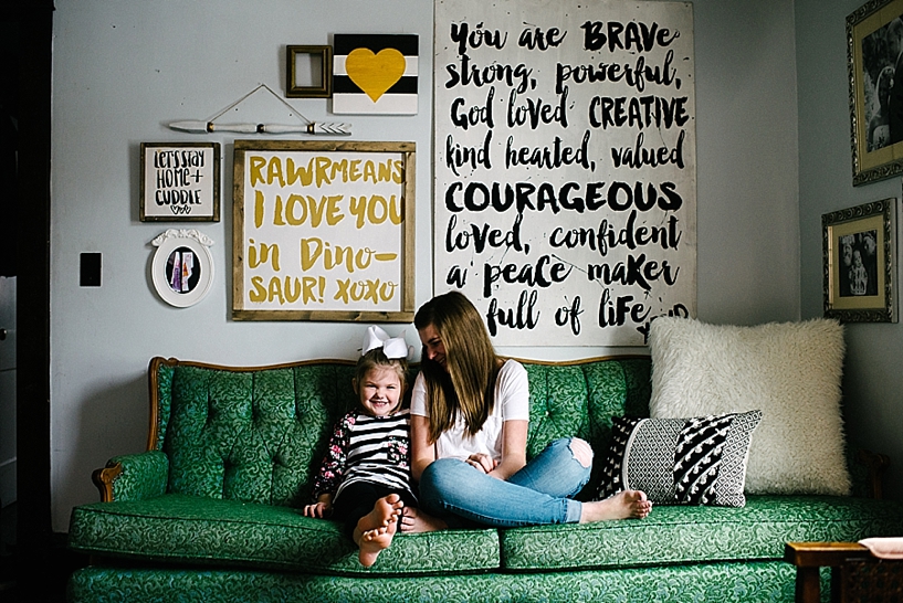 two sisters sitting on vintage green sofa with hand lettered signs hanging on the wall