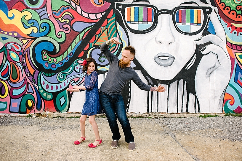 young daughter and her father bumping hips in front of colorful graffiti mural wall