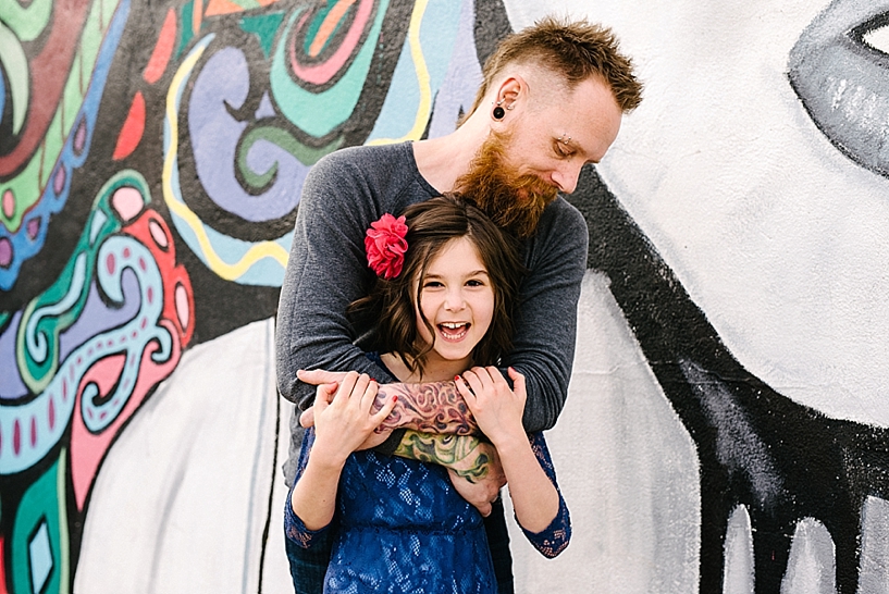 dad with beard and mohawk and piercings hugging young daughter wearing blue lace dress