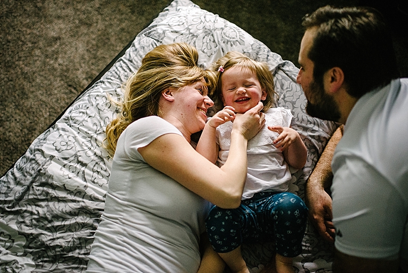 mom and daughter laying on bed laughing with dad nearby