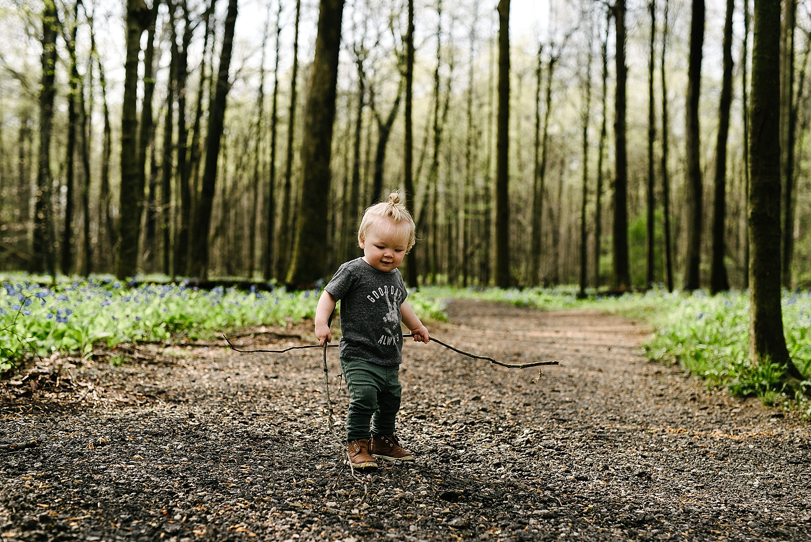 hipster toddler wearing man bun standing in woods holding sticks