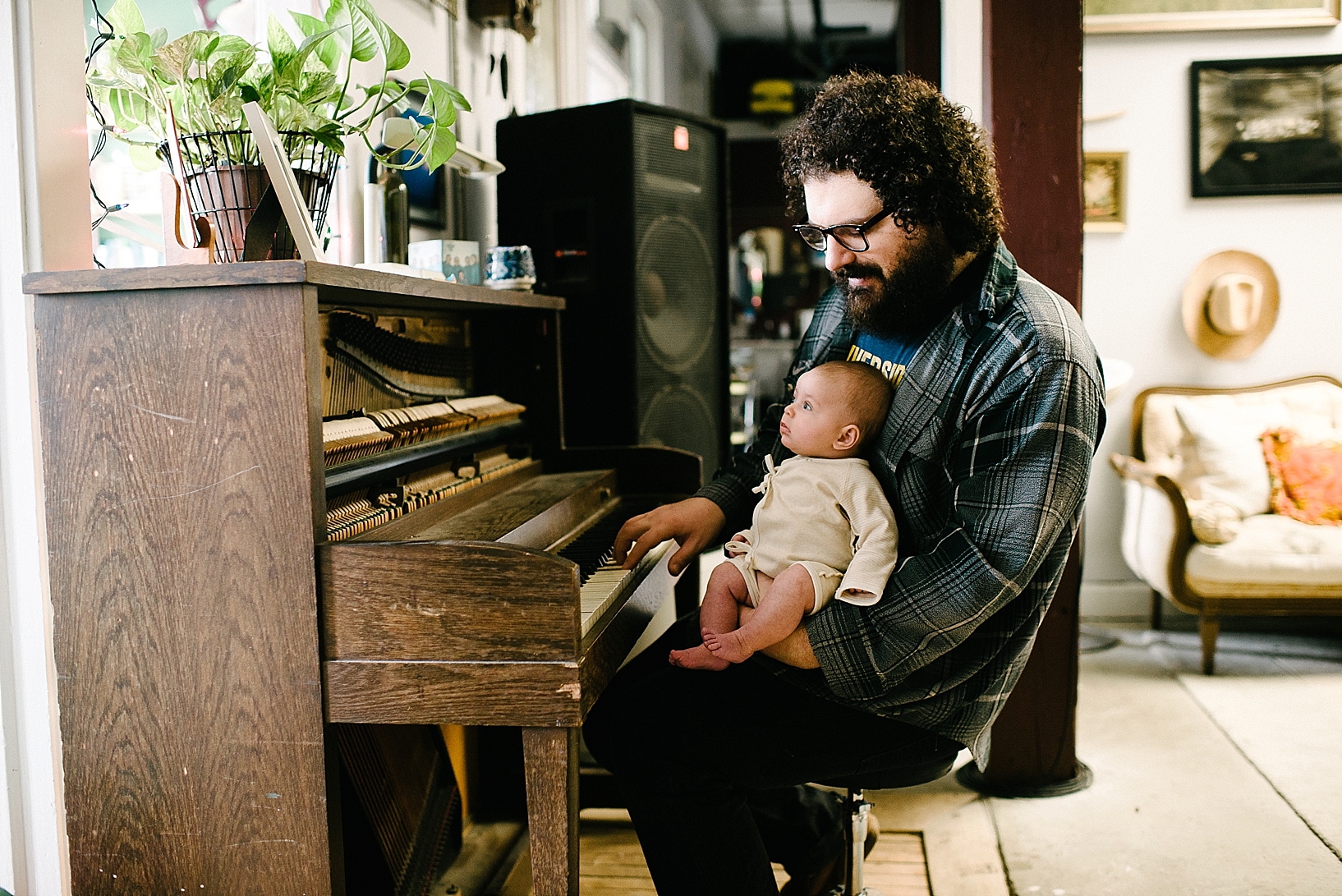 Sam Goodwill sitting at piano holding infant daughter
