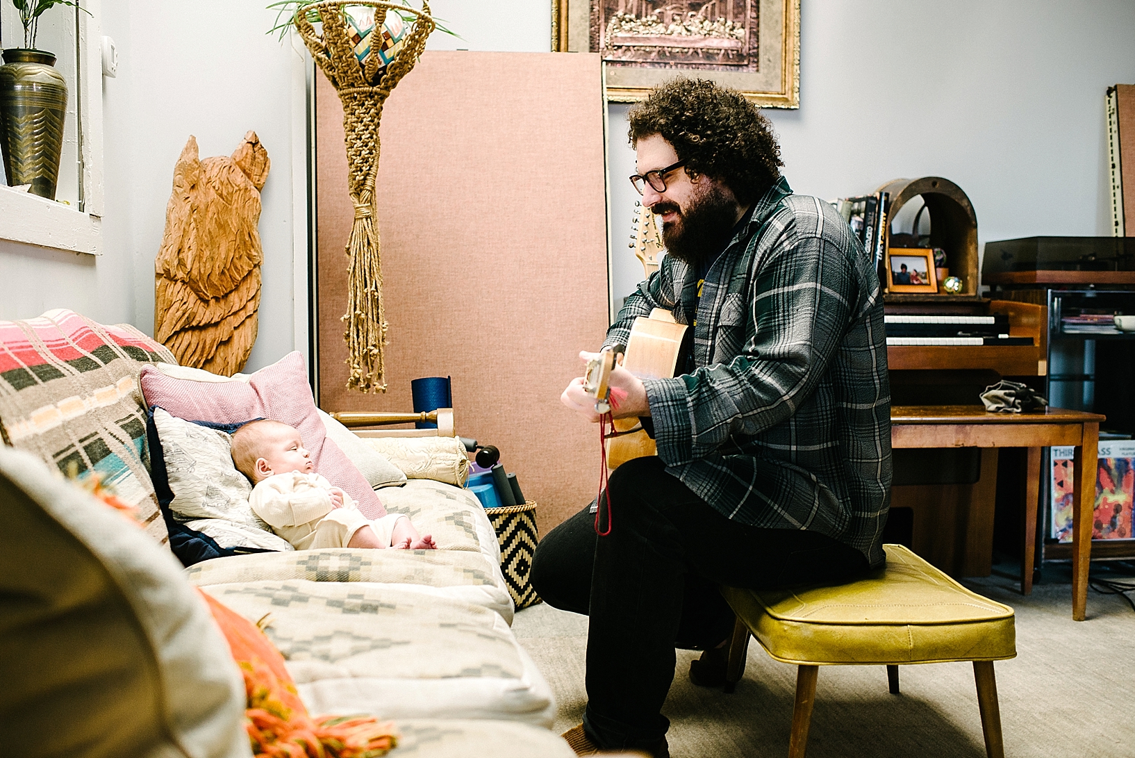 man playing acoustic guitar for baby daughter sitting on couch