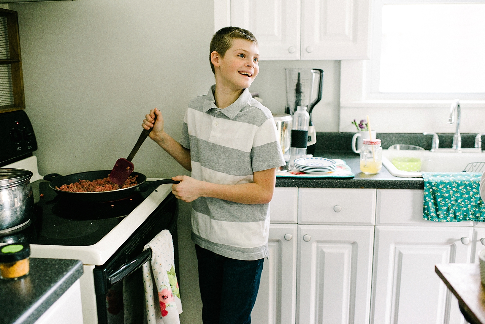 pre-teen boy standing at oven cooking meat in skillet