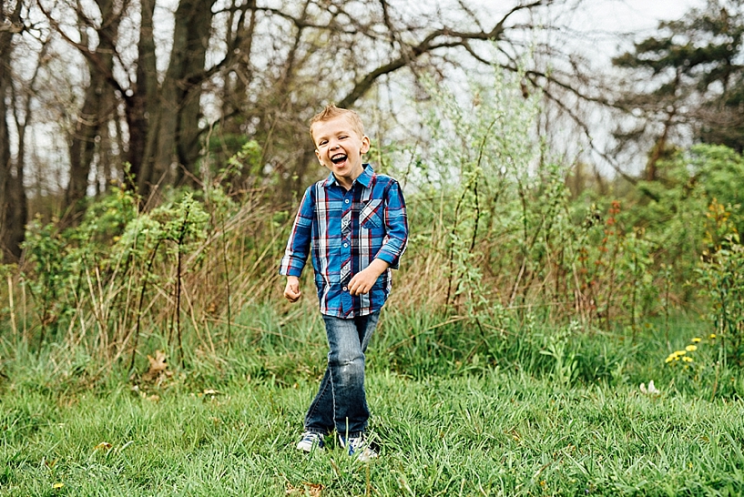 young boy wearing jeans and blue plaid shirt laughing in field