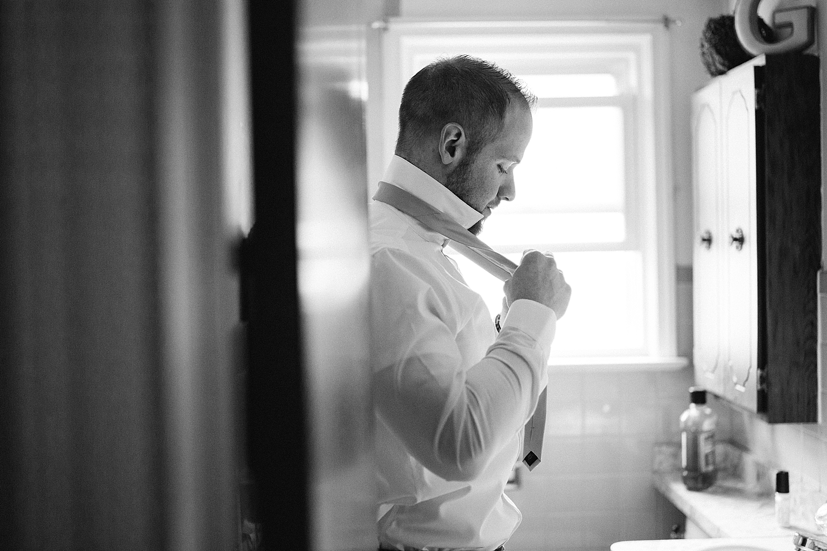 groom tying tie in bathroom mirror