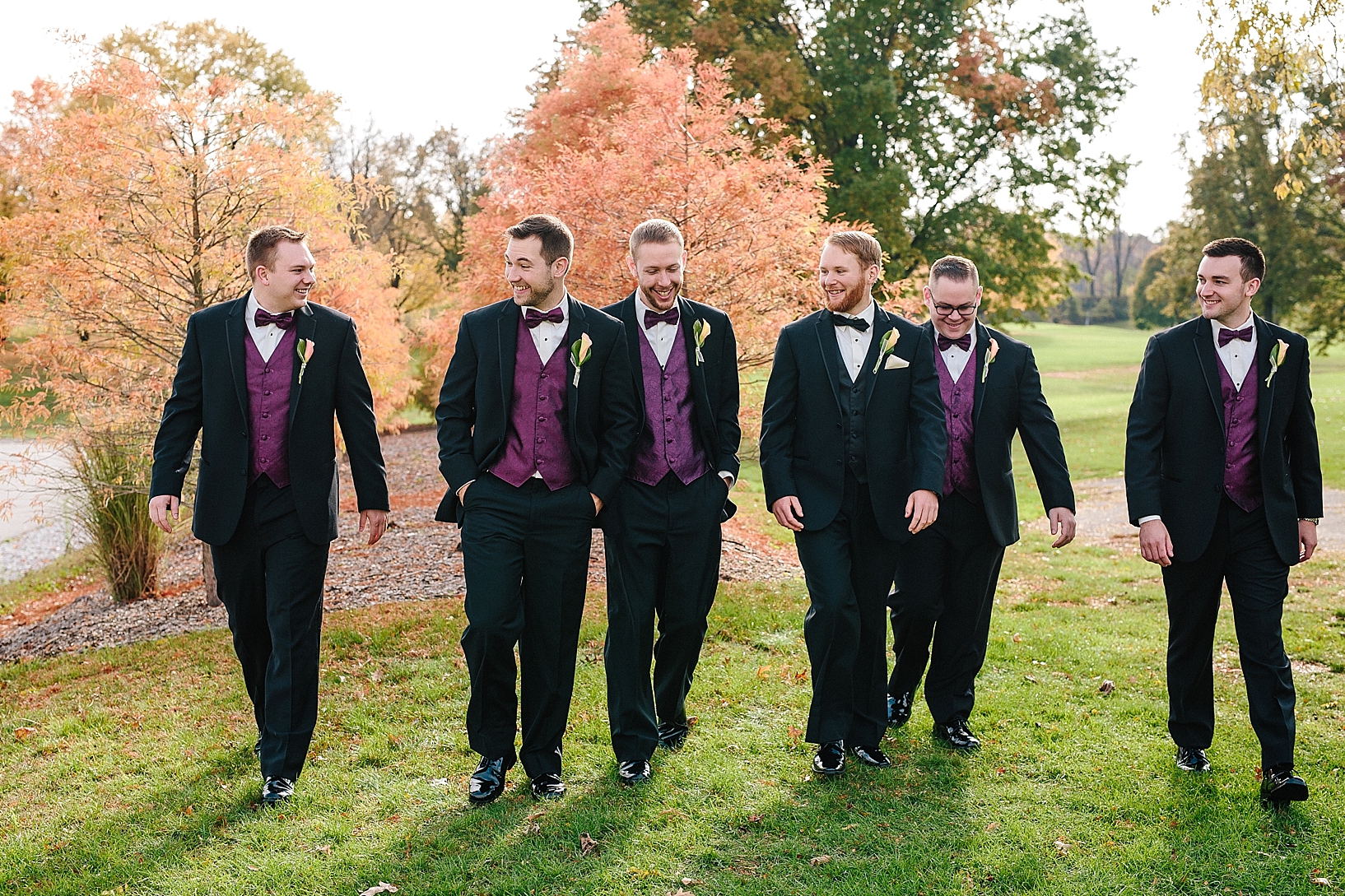 groomsmen in tuxes and wine vests walking across lawn
