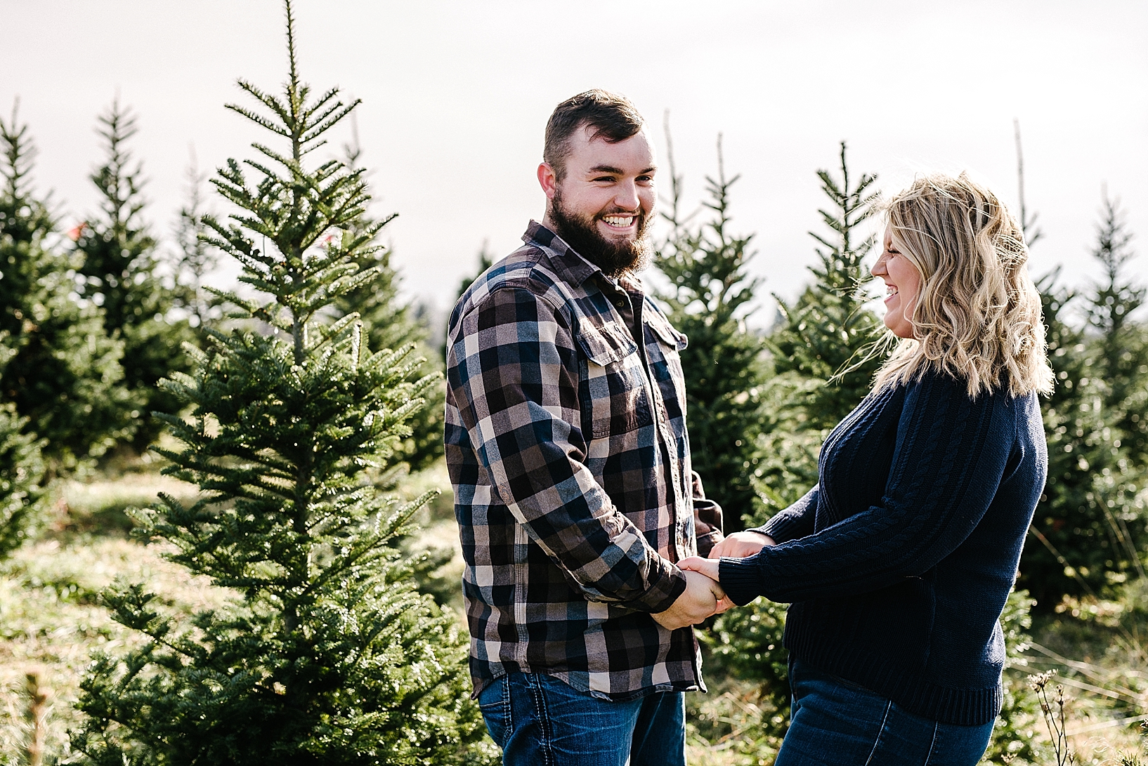 couple holding hands and laughing at tree farm