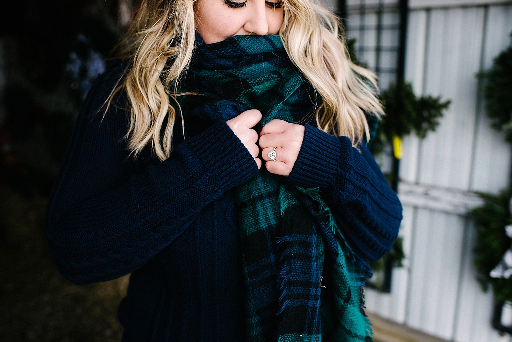 woman with blonde hair wearing blue sweater and blanket scarf with diamond engagement ring