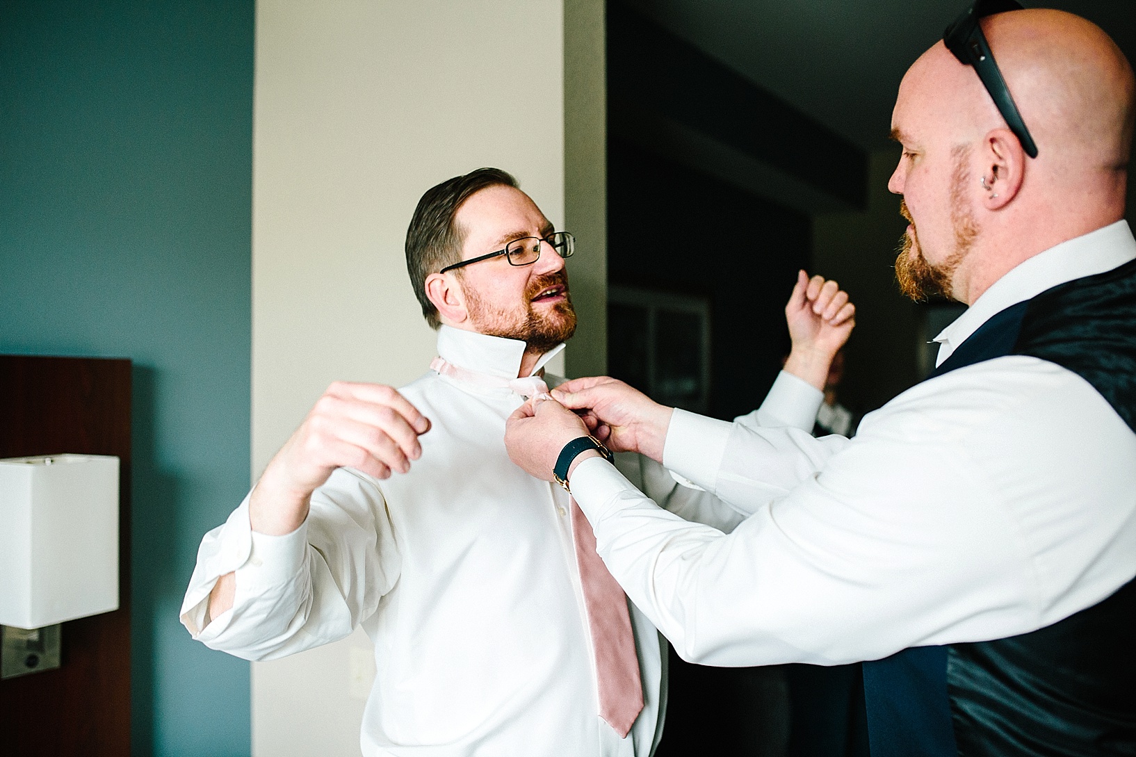 groomsmen helping groom get dressed in hotel room