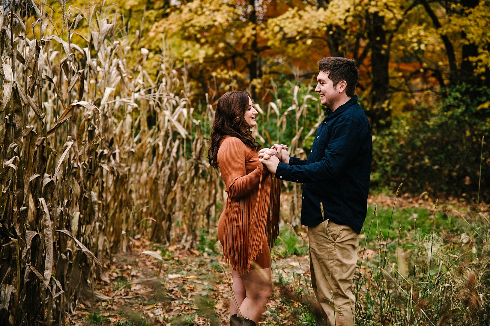 couple holding hands and smiling standing next to corn field in autumn
