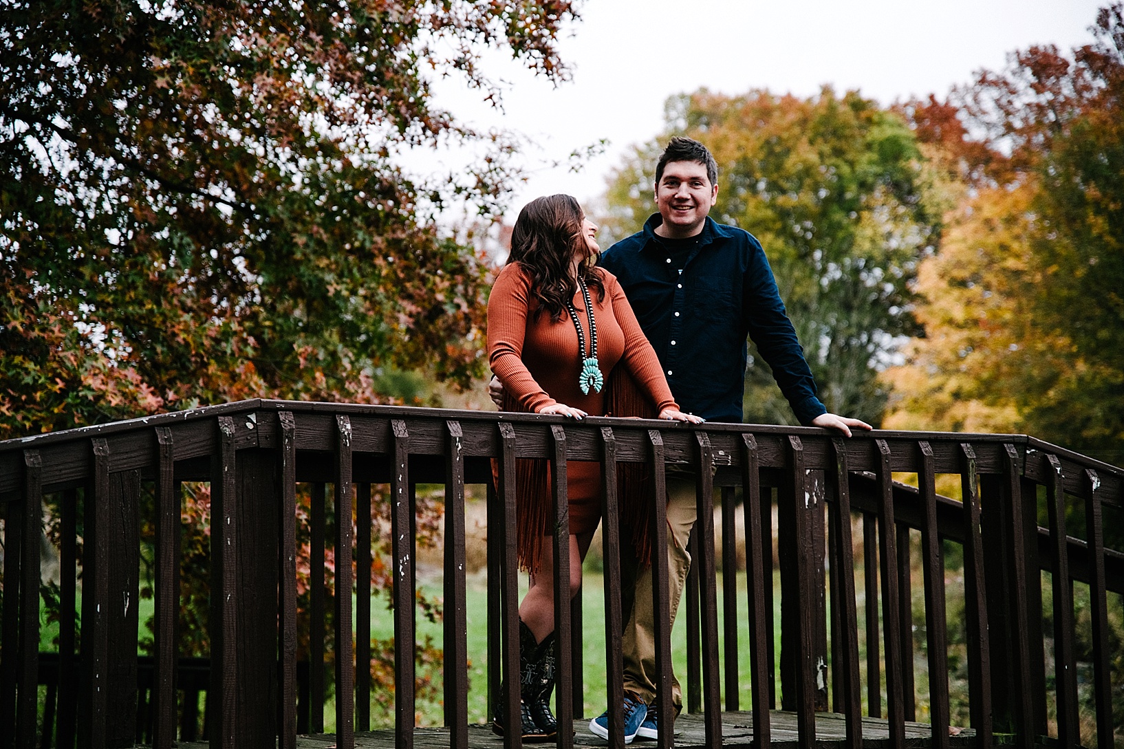 couple standing on wooden bridge with autumn trees in background
