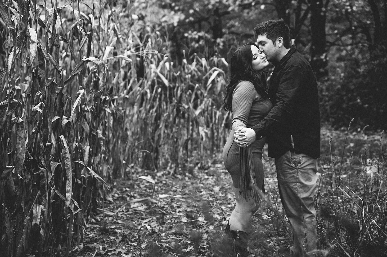 black and white photo of man kissing woman on cheek in front of corn field