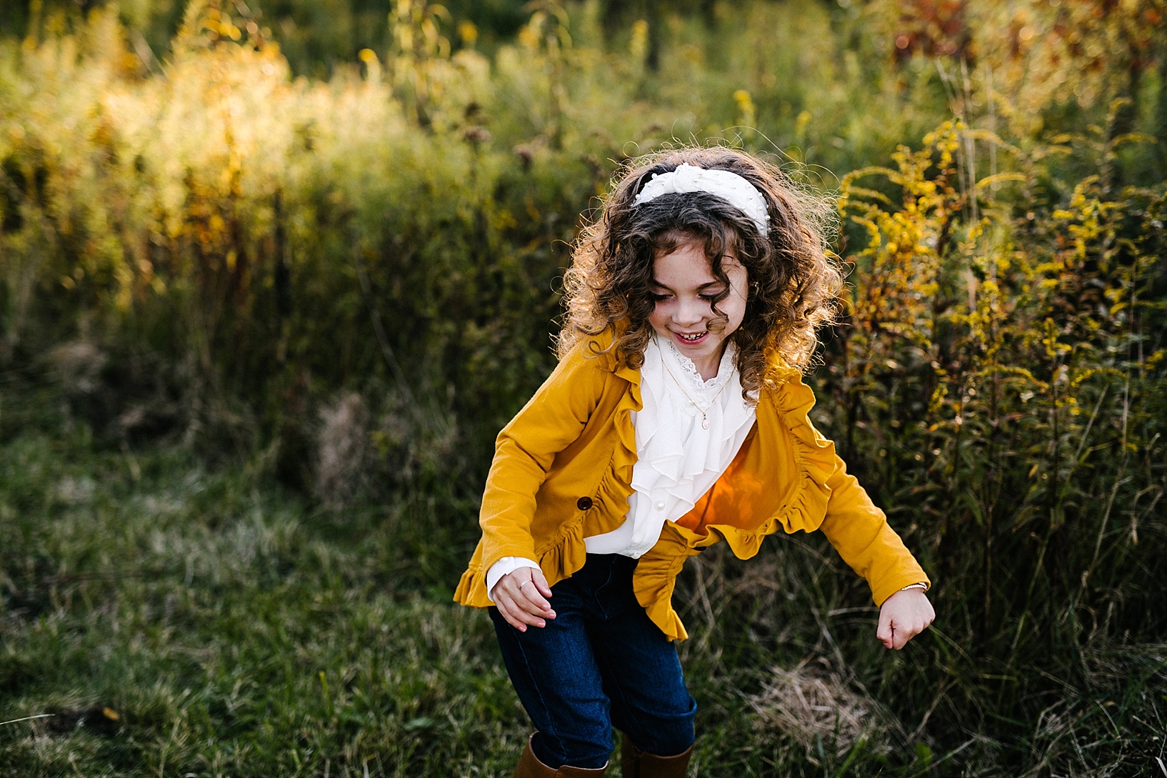 little girl in mustard yellow sweater dancing in field